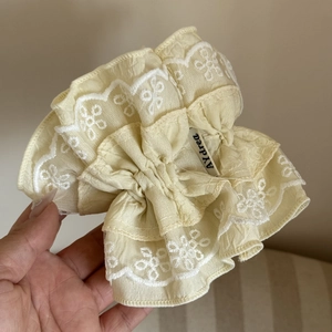 Close-up of pale yellow lace scrunchie with layered pleats and white floral embroidery