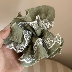Close-up of grey-green scrunchie with detailed white floral lace embroidery and soft texture