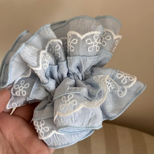 Detail of light blue lace scrunchie with intricate floral embroidery and pleated fabric texture
