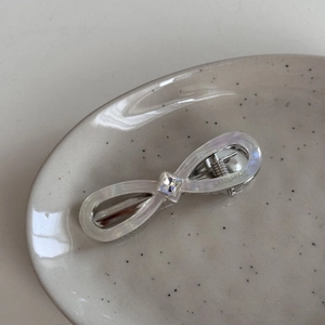 Detailed macro view of white acetate bow hair clip with square crystal in a ceramic dish