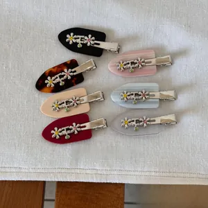 Flat lay of seven colorful resin flower hair clips with sparkling rhinestones on white linen