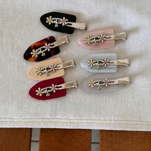 Set of six metal flower acetate hair clips in assorted colors on a soft fabric background