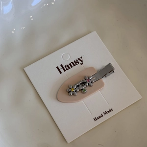 Detail of metal flower hair clip with pink and green rhinestones on display card