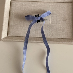 Detail of blue plaid bow hair clip with long ribbons and small black claw attachment