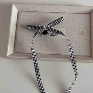 Detail of checkered bow hair clip with long ribbons on a minimalist display box