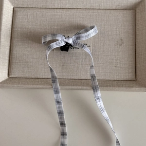 Detail showing the black and white plaid bow hair clip with long elegant ribbons on beige linen