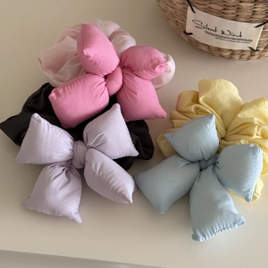 Close-up of colorful 3D bow scrunchies in pink, purple, and blue on a beige background