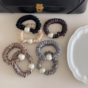 Detail of five silk satin scrunchies in neutral colors featuring large central pearls
