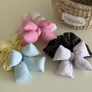 Detail view of four colorful padded bow scrunchies in pink, yellow, blue, and grey fabric