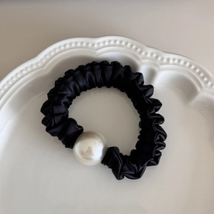 Elegant black satin hair scrunchie with white pearl detail on a white ceramic tray