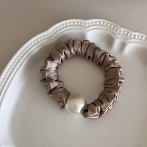 Detail view of smooth champagne satin hair scrunchie featuring an elegant large white pearl