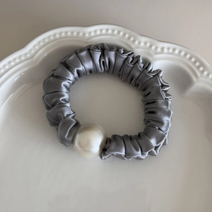Close-up of silver-grey satin scrunchie with large pearl detail in a white porcelain dish