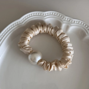 Detailed close-up of a champagne satin scrunchie with a large pearl on a ceramic tray