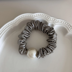 Detailed view of silver grey satin scrunchie with large pearl on white ceramic tray