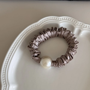 Detailed close-up of a champagne silk scrunchie with a large pearl on a ceramic plate