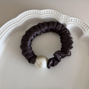Detail of a brown satin scrunchie featuring a large elegant pearl on a white plate