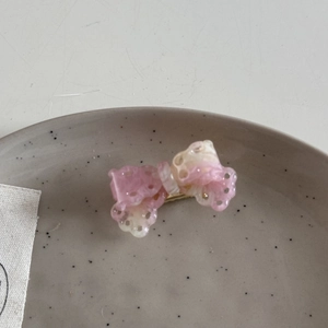 Close-up of a pink acetate bow hair clip with hollow-out details on a ceramic dish
