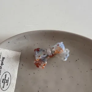 Close-up of acetate hollow bow hair clip with orange and blue marbled texture on ceramic plate