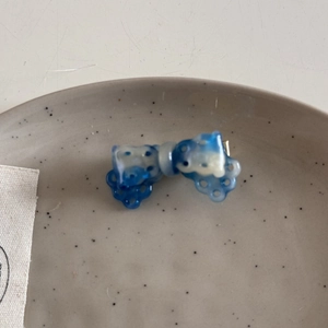Close-up of a blue and white acetate bow hair clip with textured patterns in a ceramic tray