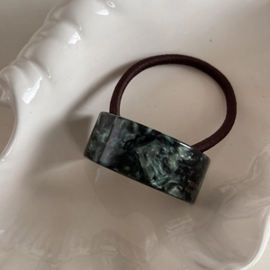 Detail of dark green marble pattern acetate hair tie with gold handmade engraving