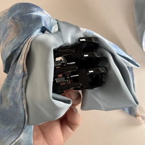 Détail de la pince à cheveux en satin bleu clair avec motif peinture à l'huile