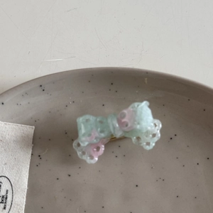 Close-up of a mini acetate bow hair clip with translucent weave texture in green and pink