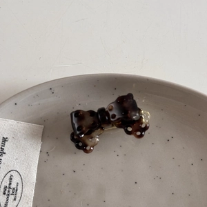 Detail view of mini acetate bow hair clip with dark tortoiseshell pattern on ceramic plate