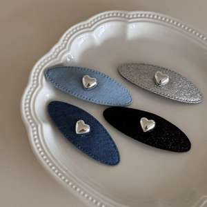 Dettaglio di quattro fermagli ovali in denim e glitter con cuori in metallo su un piatto bianco