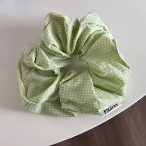 Detail view of light green checkered fabric scrunchie with a white woven logo tag