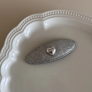 Dettaglio del fermaglio per capelli ovale con glitter argento e cuore metallico