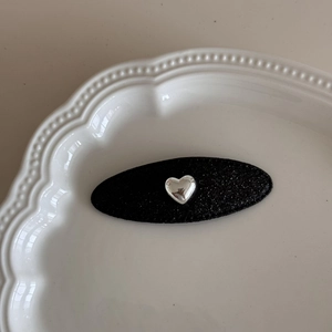 Dettaglio di fermaglio nero ovale con cuore argento su vassoio di ceramica bianca