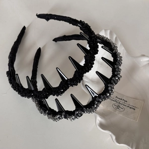 Détail d'un serre-tête punk avec pointes noires et perles de cristal sur coquille blanche