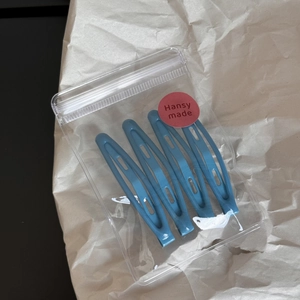 Detail of 4-piece matte blue hair clip set in transparent pouch with brand sticker