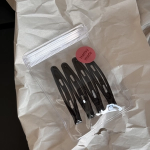 Pack of four glossy black teardrop-shaped metal hair clips in minimalist packaging