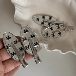 Detail of silver alloy hair clips with black bow patterns on a white ceramic dish