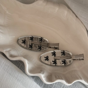 Minimalist silver mirror hair clips with black bow patterns on a ceramic shell tray