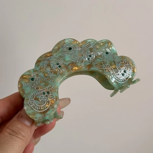 Detail of vintage petal hair claw with green marble texture and silver vine carvings