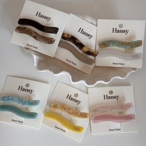 Détail de barrettes à cheveux ondulées en acétate coloré sur une carte de présentation