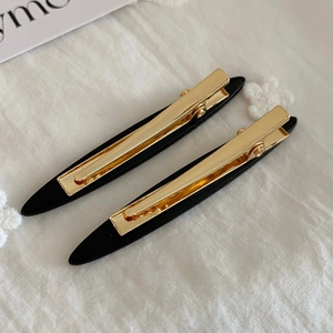 Detailed macro view of two minimalist black acetate hair clips with gold metal duckbill grips