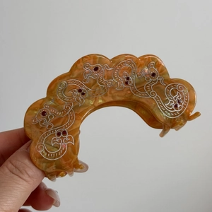 Detail showing amber acetic acid hair claw with silver dragon motif and red rhinestones