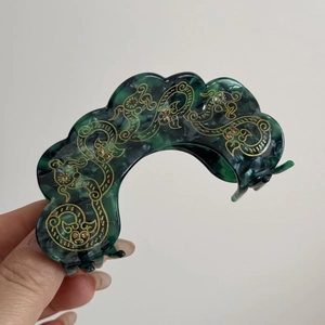 Detail of vintage hair claw with dark green marble pattern and golden cloud patterns