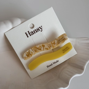 Détail de barrettes ondulées en acétate beige marbré et jaune sur un plateau coquille