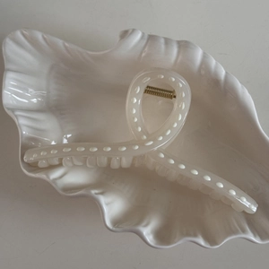 Detail shot of a white translucent hair claw clip with elegant ribbon-style cross design
