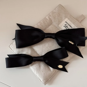 Elegant set of two black satin bow hair clips with gold metal tags on beige fabric