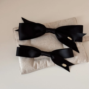 Set of two black satin bow hair clips with elegant gold oval charms in minimalist style