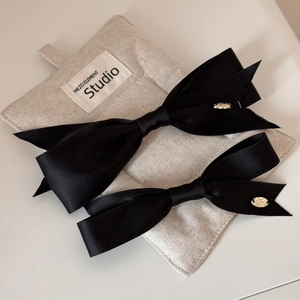 Detail of elegant black satin bow hair clips with gold metal tags on a gray linen pad