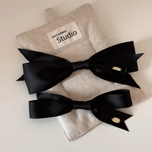 Detailed close-up of two black satin bow hair clips in large and small sizes with metal tags