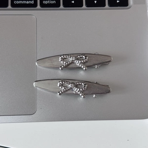 Detail of two silver brushed metal hair clips featuring delicate bow patterns