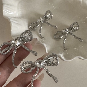 Détail des barrettes nœud argentées avec strass et cristaux posées dans un plat en céramique