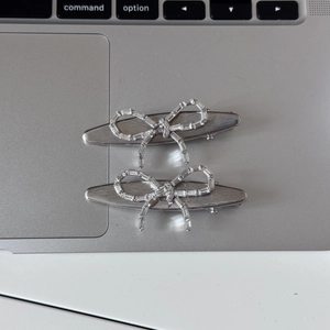 Close-up of silver bow hair clips with emerald-cut crystals on a sleek surface